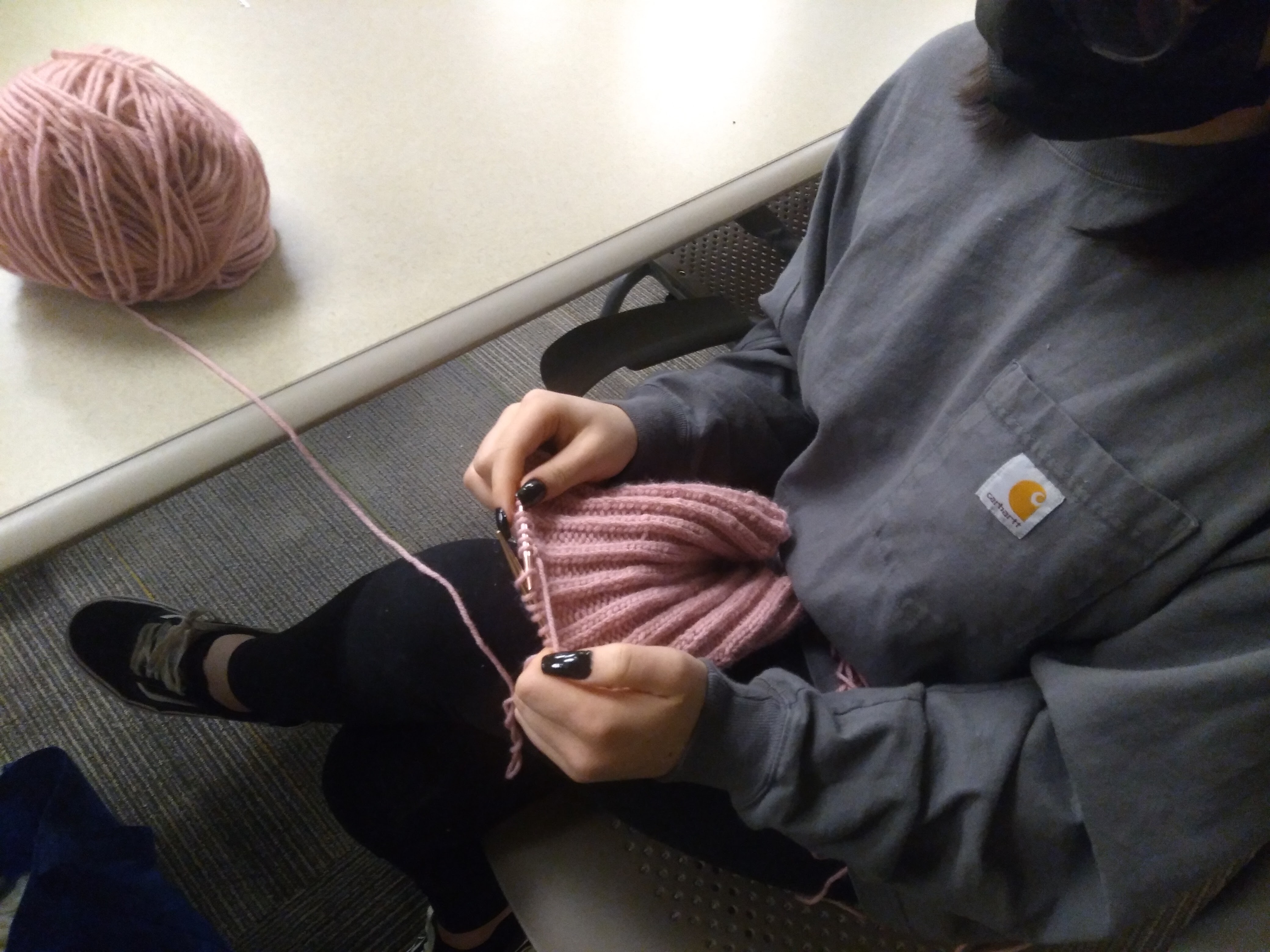 A student knits a beanie for an Afghan refugee family