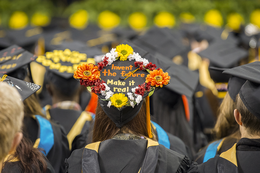 A VCU graduate sits at graduation with a cap that reads Invent the Future make it real