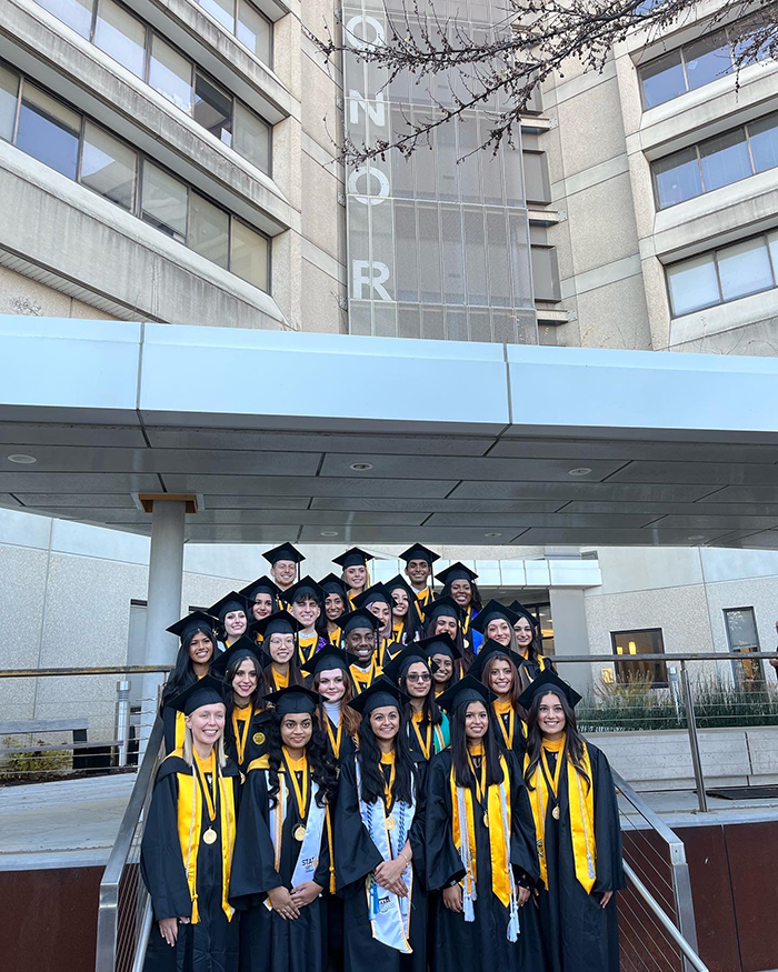 The Honors Fall 2022 graduating class stadning in front of the Honors College building wearing full regalia