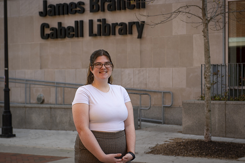 A woman wearing a white top and brown pants stands in front of Cabell Library on V C U's Monroe Park campus