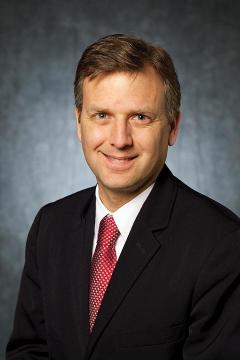 A man wearing a black suit jacket, white dress shirt and red tie.