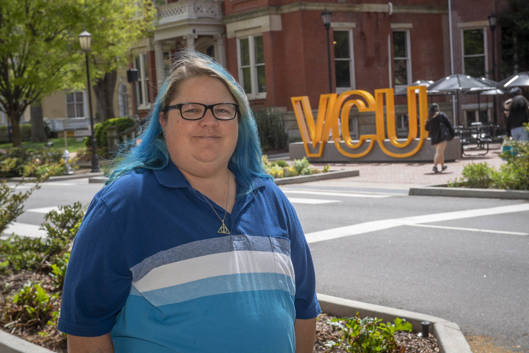 A person with dyed blue hair wearing a blue shirt in front of the V C U sign on Franklin St